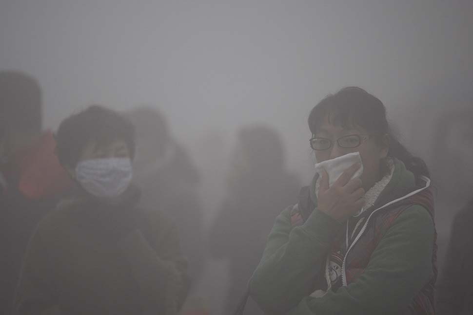 Commuters cover their mouths while waiting for buses in the heavy fog and smog in Harbin, China on Monday.