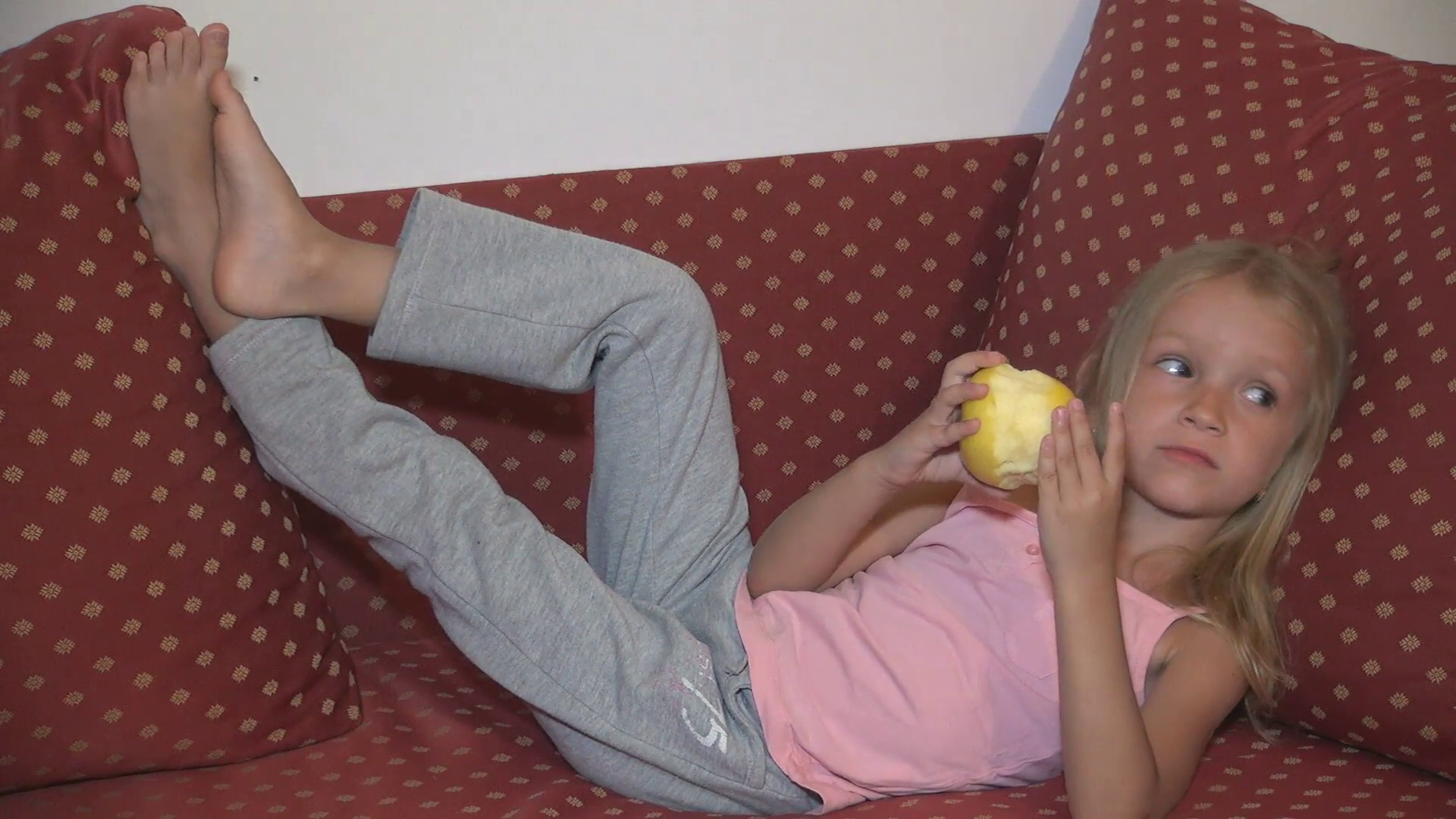 girl-eating-apple-fruit-on-sofa-child-taking-snack-breakfast-while-watching-tv_4ppw591ae__F0010