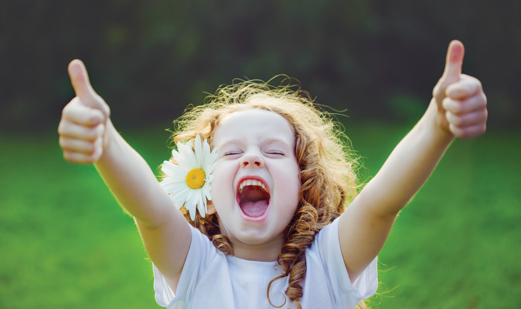 Laughing girl with daisy in her hairs, showing thumbs up.