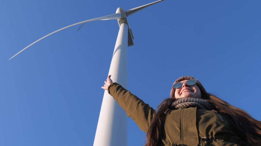 videoblocks-energy-production-smiling-girl-is-having-fun-and-waving-arms-under-wind-power-turbines-close-up-against-sky-bottom-view_rus1zo6nm_thumbnail-full01
